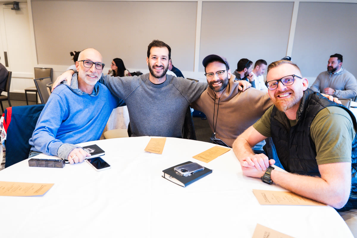 Four doctors at a round table with arms around each other, smiling